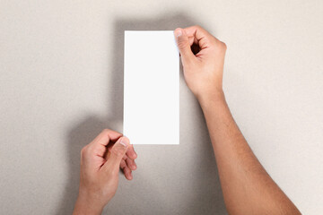 Man holding flyer on grey background, closeup. Mockup for design