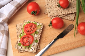 Fresh crunchy crispbreads with cream cheese, tomatoes and avocado on beige table, above view