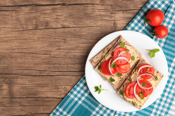 Fresh crunchy crispbreads with pate, tomatoes, red onion and greens on wooden table, flat lay. Space for text