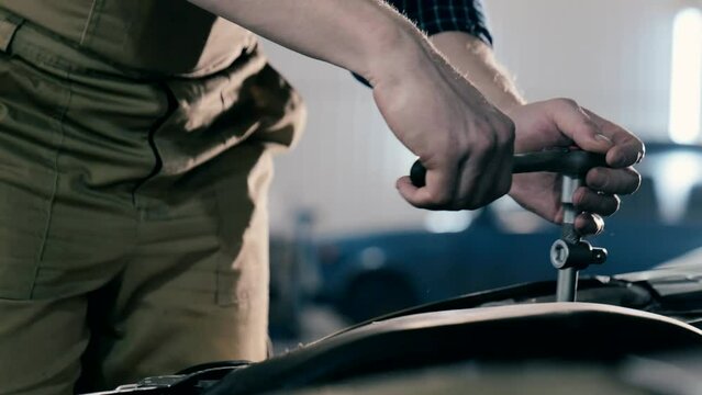 An auto mechanic is working on a car engine in a car workshop. Close-up ratchet wrench