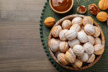 Bowl of delicious nut shaped cookies with boiled condensed milk on wooden table, flat lay. Space for text