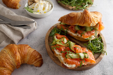 Croissants with cheese cream, red fish and cucumber on a wooden stand served for breakfast or lunch