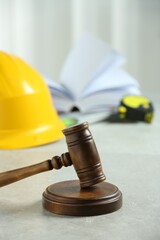 Construction and land law concepts. Judge gavel, construction helmet, tape measure and open book on light grey table