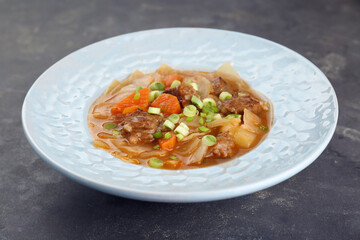 Tasty cabbage soup with meat, green onion and carrot on grey table, closeup