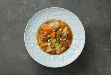 Tasty cabbage soup with meat, green onion and carrot on grey table, top view