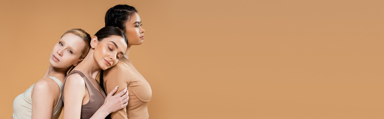 sensual blonde woman looking at camera near multiethnic models posing in underwear isolated on...