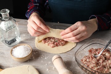 Woman making chebureki with meat at wooden table, closeup