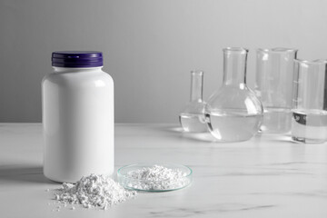 Calcium carbonate powder, jar and laboratory glassware on white marble table. Space for text