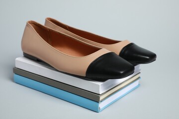 Stack of books with pair of new stylish square toe ballet flats on light grey background