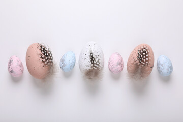 Many painted Easter eggs with feathers on white background, flat lay