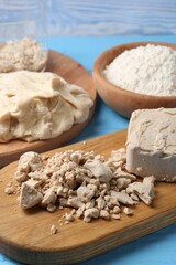 Compressed yeast, dough and flour on light blue wooden table, closeup