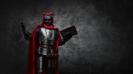 Shot of mysterious cultist dressed in steel armor and red mantle holding book.