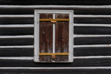 Wooden window shutter on traditional mountain cottage with brown and white facade