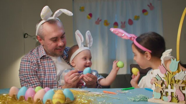 Easter holiday. Happy family, father and children and a baby boy color and decorate eggs cheerfully for the Easter holiday. Happy family painting Easter eggs