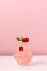 Raspberry drink with ice in glass on pink background. Refreshing tropical summer berry lemonade or...