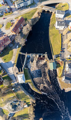 Fototapeta premium Aerial view on a big dam, barrage, weir in a city near a green area on a sunny day. Panorama of a river, water flowing.