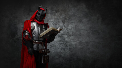 Shot of mysterious cultist dressed in steel armor and red mantle holding book.