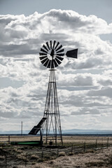 Windmill on the plains, powered by solar panels with livestock watering tank by barbed wire fence...