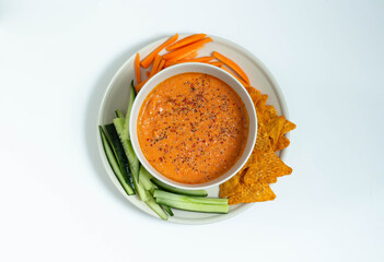 Sauce in a round bowl on a plate with carrots, cucumber and chips. Top view.