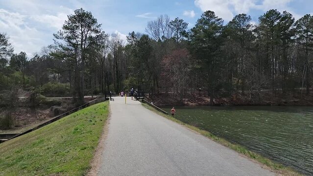 footage along the banks of Lawrenceville Lake with men fishing and a woman walking along the footpath wearing a pink shirt at Rhodes Jordan Park in Lawrenceville Georgia USA