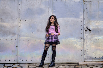 Teenage girl dressed in gothic style posing standing in front of a metal gate