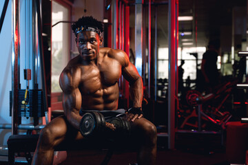 20s Black and muscular man in a gym doing concentration curls with dumbbell