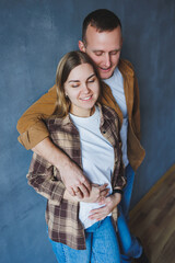 Happy couple in love dressed in shirts, standing on the background of gray wall, looking at empty space, isolated background of gray concrete wall. The concept of a happy couple in love.