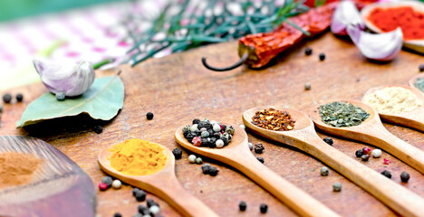 Spices in wooden spoons and herbs on wooden table close up

