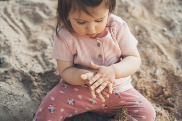 A little baby girl with bare feet sitting on the ground and playing with sand. Kid enjoying the sunny day in the country garden.