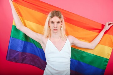 Young gay man 20s with make up wrapped in rainbow striped flag isolated on background, studio portrait. People lifestyle fashion lgbtq concept.