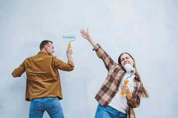 Young married couple in love in shirts and jeans doing renovations, renewing painting walls with a...