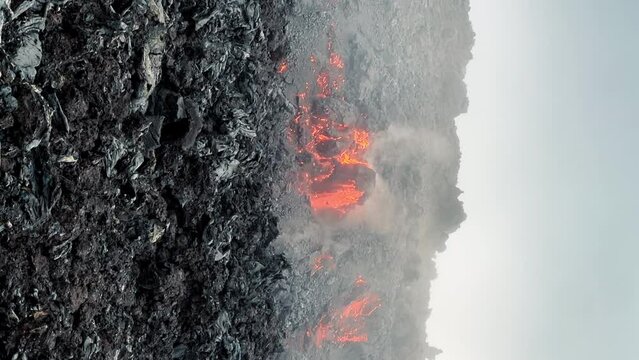 Epic vertical shot on smartphone camera of red hot lava flowing and freezing with smoke in black coals. Smoke surface of active volcano on Hawaii Island in Pacific ocean USA incredible wilderness trip