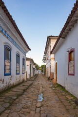 Fototapeta na wymiar Paraty, Rio de janeiro, Brazil. Old street and houses from the colonial period. Stone street floor. Background blue sky.