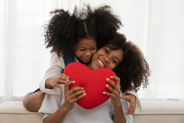 Happy afro family embracing together and surprise with pillow heart shape on sofa at home. Smiling...