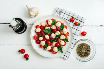 Naklejka na ściany i meble Italian caprese salad with cherry tomatoes, mozzarella, basil, garlic, balsamic sauce on a white wooden table. Top view, flat lay