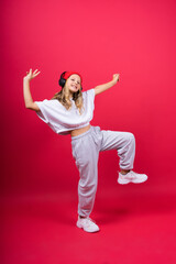 Fototapeta premium Girl listening to music in headphones on red background. Cute child enjoying dance music, smile