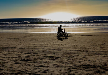 People biking on beach, silhouette, in golden sunset.