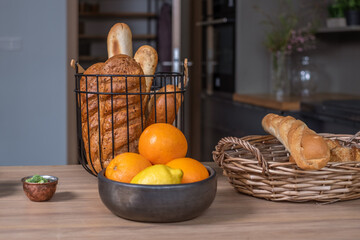 Obraz na płótnie Canvas Two baskets with bread and French baguettes on a wooden kitchen table with a kitchen in the background, a bowl of oranges. food advertising poster,