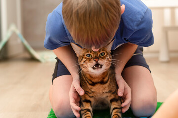 People. Health concept. A boy and a domestic bengal cat are engaged on a massage orthopedic multi-colored rug in the home interior. Treatment of flat feet. - Powered by Adobe