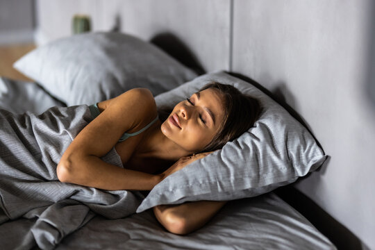 Sleeping young woman lies in bed with eyes closed.