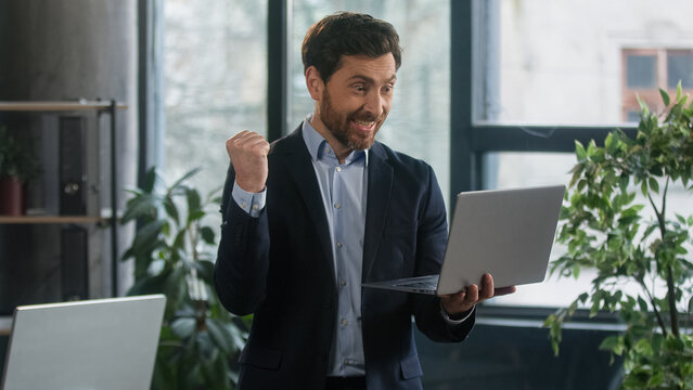 Happy excited businessman in office checking email on laptop read good news man winner successful entrepreneur receive reward bonus celebrating business success victory financial market growth concept