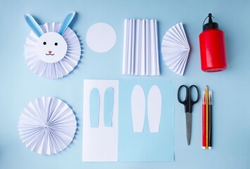 Easter layout on the table on a blue background, a children's craft for the Easter holiday, a cute, cute white rabbit.  Component crafts and accessories.  Flat lay.  Easter holiday concept.