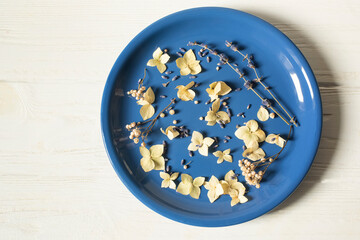 Blue plate with dry flowers on a white wooden background.