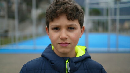 Portrait of a serious young boy standing outdoors looking at camera. Preteen male kid stands at park during winter season with serious expression