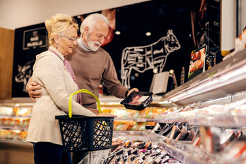 An old couple is buying fresh packed meat at butchery in supermarket.