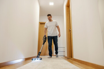 A man is vacuuming hallway at home.