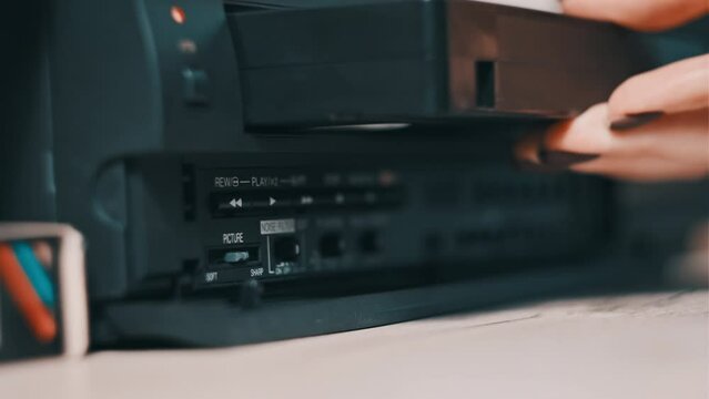 Insert VHS cassette into VCR player. Black vintage videotape cassette recorder on a desk with many archived video cassettes. Female hand inserting old VHS Tape into retro player. Home video, nostalgia