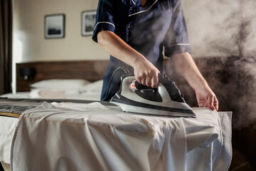 Close up of a maid ironing shirt in a hotel room.