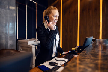 A happy receptionist is answering guest's call from a hotel in reception.