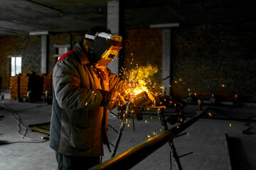 Fototapeta na wymiar Construction of a production facility. The master performs welding and grinding at his workplace. Man in protective helmet and gear